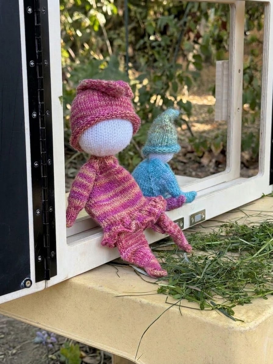 Zwei gestrickte Figuren sitzen am entnommenen Bildschirmrahmen des eKami – das eKami als Puppentheater.