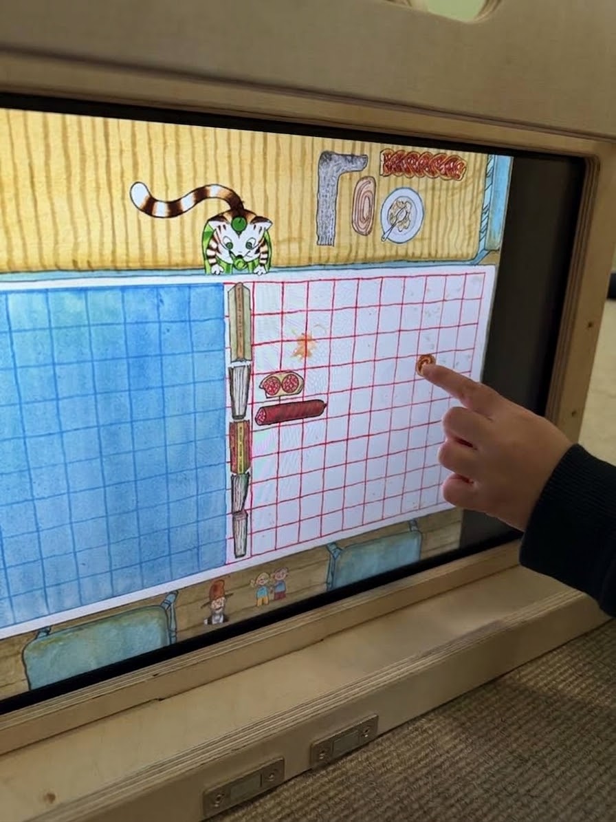 Ein Kind spielt auf dem Touchscreen des eKami „Frühstück versenken“ aus „Findus 4 – Findus bei den Mucklas“.