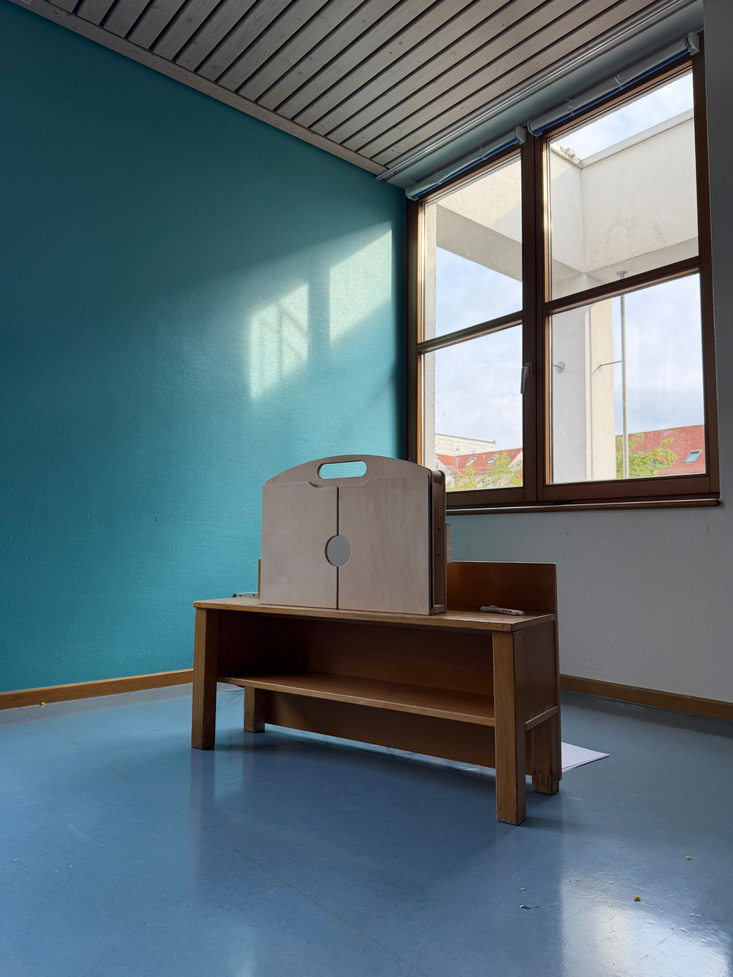 Das zusammengeklappte eKami mit Tragegriff steht auf einem Tisch vor einer türkisfarbenen Wand.