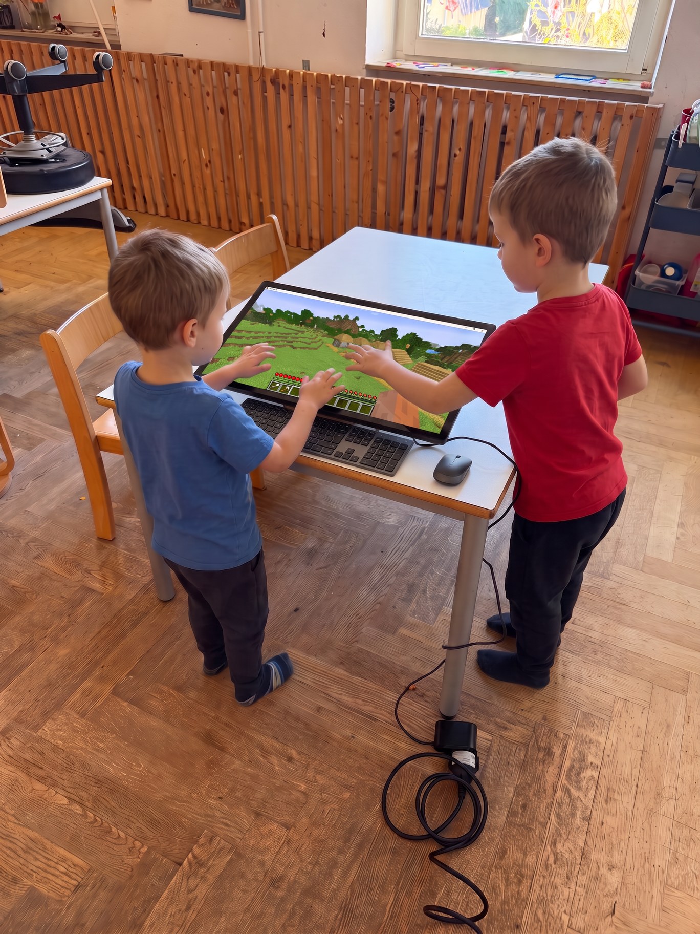KI-bearbeitetes Originalfoto: Zwei Schulkinder spielen Luanti am eKami-Touchscreen im Schülerhort. Der Bildschirm mit schwarzem Rand liegt wie im Original leicht geneigt auf dem weißen Tisch, davor liegen Tastatur und Maus, auf dem Bildschirm ist eine Blocklandschaft zu sehen.